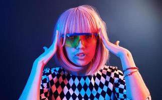 porträtt av ung flicka med blond hår i glasögon i röd och blå neon i studio foto