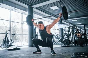 stark ung man i sportigt kläder håller på med övningar med tung vikter i de Gym foto