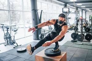 stark ung man i sportigt kläder och skrämmande mask håller på med skjuta på Posten på ett ben i Gym foto