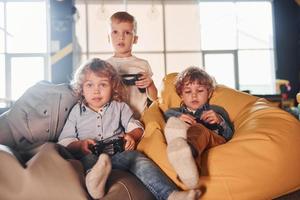 barn i tillfällig kläder Sammanträde tillsammans med kontrollant och spelar video spel foto