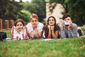 lekfull humör. grupp av ung studenter i tillfällig kläder på grön gräs på dagtid foto