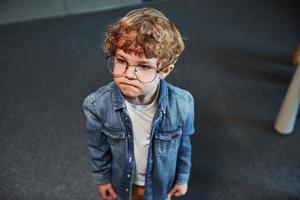 porträtt av söt unge i glasögon den där stående inomhus foto