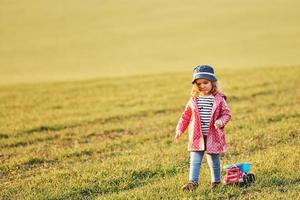 söt liten flicka promenader med leksak bil på de skön fält på solig dagtid foto