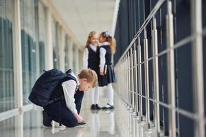 pojke Sammanträde på de golv. skola barn i enhetlig tillsammans i korridor foto