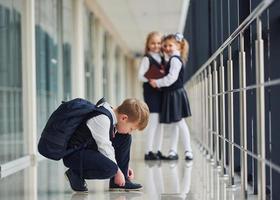 pojke Sammanträde på de golv. skola barn i enhetlig tillsammans i korridor foto