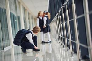 pojke Sammanträde på de golv. skola barn i enhetlig tillsammans i korridor foto