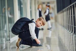 pojke Sammanträde på de golv. skola barn i enhetlig tillsammans i korridor foto