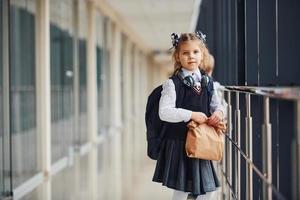 ung liten skola flicka i enhetlig stående i hall med paket av middag i händer foto