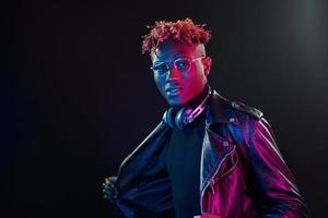 Framställ med trådlös hörlurar på nacke. trogen neon belysning. ung afrikansk amerikan man i de studio foto