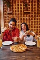 mång etnisk ung par Sammanträde inomhus tillsammans och äter pizza foto
