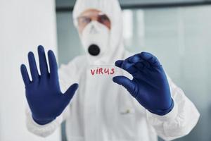 manlig läkare forskare i labb täcka, defensiv glasögon och mask innehar glas med virus ord på den foto