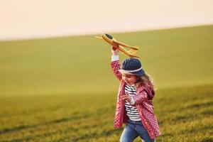 söt liten flicka ha roligt med leksak plan på de skön grön fält på solig dagtid foto