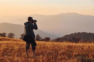 manlig fotograf stående och arbetssätt på majestätisk landskap av höst träd och bergen förbi de horisont foto