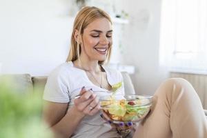 porträtt av attraktiv caucasian leende kvinna äter sallad. kvinna äter friska sallad med tomater körsbär inomhus friska livsstil foto