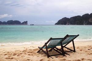 resa till ö phi phi, thailand. två stolar på en strand nära till hav. foto