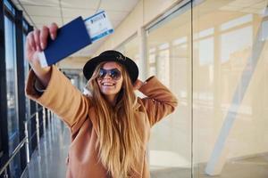 ung kvinna passagerare i värma kläder som visar biljetter i flygplats hall foto