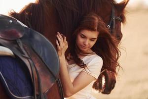 ung kvinna fattande henne häst i lantbruk fält på solig dagtid foto