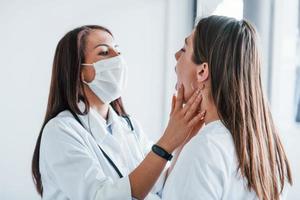 kontroll lymfa knutpunkter och hals. ung kvinna ha en besök med kvinna läkare i modern klinik foto
