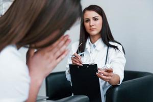 läkare ger läkemedel till gråt patient. ung kvinna ha en besök med kvinna läkare i modern klinik foto