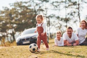 Lycklig familj spelar med fotboll boll utomhus nära de skog. med dotter och son foto