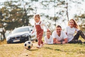 Lycklig familj spelar med fotboll boll utomhus nära de skog. med dotter och son foto
