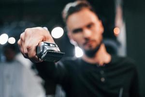 ung skäggig man stående i barberare affär och innehav klippare foto