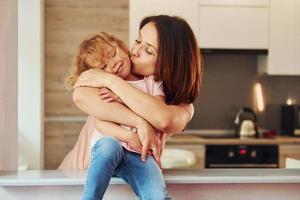 på de kök. ung mor med henne liten dotter i tillfällig kläder tillsammans inomhus på Hem foto