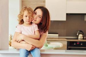 på de kök. ung mor med henne liten dotter i tillfällig kläder tillsammans inomhus på Hem foto