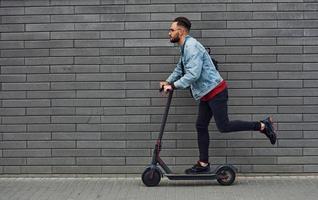 sida se av stilig ung kille i tillfällig kläder den där ridning elektrisk skytt utomhus på solig dagtid foto