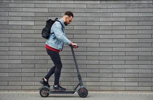 stilig ung kille i tillfällig kläder ridning elektrisk skytt utomhus på solig dagtid foto