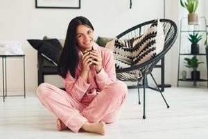 glad ung kvinna i pyjamas Sammanträde på de golv inomhus på dagtid foto