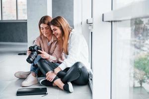 två kvinnor Sammanträde inomhus tillsammans och utseende på foton på de kamera