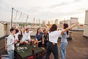 grupp av ung människor i tillfällig kläder ha en fest på taket tillsammans på dagtid foto