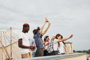 dekorerad plats. molnig väder. grupp av ung människor i tillfällig kläder ha en fest på taket tillsammans på dagtid foto