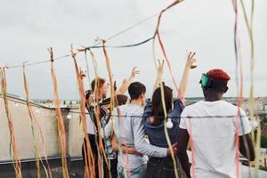 dekorerad plats. molnig väder. grupp av ung människor i tillfällig kläder ha en fest på taket tillsammans på dagtid foto