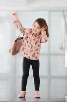 söt liten flicka med väska inomhus i de kontor eller flygplats talande förbi telefon foto