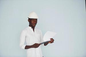 ung afrikansk amerikan ingenjör i Hardhat inomhus med anteckningsblock i händer foto