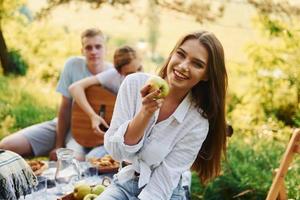 kvinna äter äpple. grupp av ung människor ha semester utomhus i de skog. uppfattning av helgen och vänskap foto