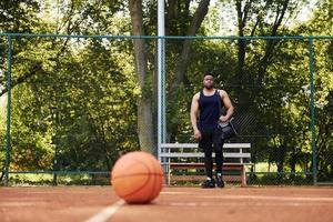 skön grön träd på bakgrund. afrikansk amerikan man spelar basketboll på de domstol utomhus foto