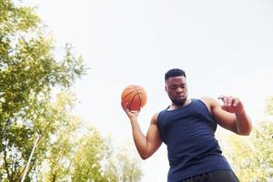 molnig väder. afrikansk amerikan man spelar basketboll på de domstol utomhus foto