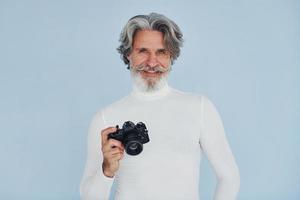 fotograf med årgång kamera. senior eleganta modern man med grå hår och skägg inomhus foto