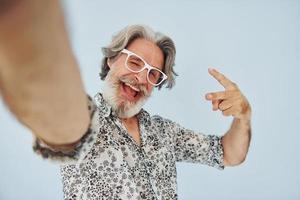 turist gör selfie. senior eleganta modern man med grå hår och skägg inomhus foto