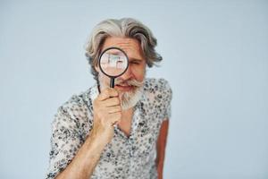 har roligt med förstorande glas. senior eleganta modern man med grå hår och skägg inomhus foto