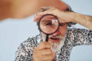 har roligt med förstorande glas. senior eleganta modern man med grå hår och skägg inomhus foto