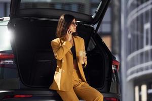 samtal förbi telefon. ung modern kvinna i vinröd färgad täcka på dagtid med henne bil foto