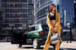 modern företag byggnad på bakgrund. ung modern kvinna i vinröd färgad täcka på dagtid med henne bil foto