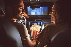 skön Lycklig ung par Sammanträde i de bil tillsammans och äter popcorn foto