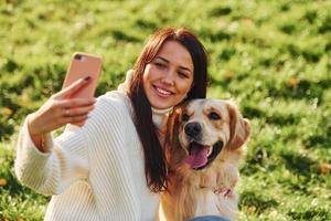 framställning selfie. ung kvinna ha en promenad med gyllene retriever i de parkera foto