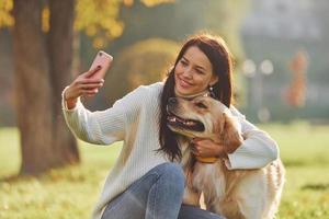 framställning selfie. ung kvinna ha en promenad med gyllene retriever i de parkera foto