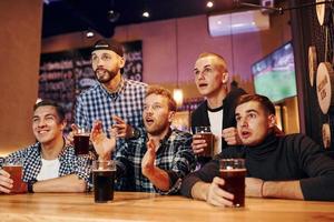 fotboll fläktar tittar på tv. grupp av människor tillsammans inomhus i de pub ha roligt på helgen tid foto